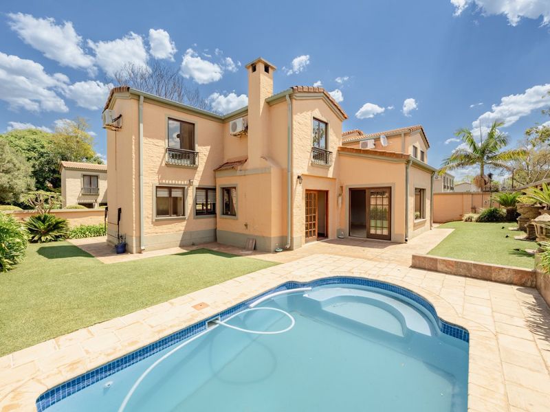 Rear view of the house featuring a swimming pool, paved patio area, landscaped garden, and multi-level exterior facade with chimney and balcony details.