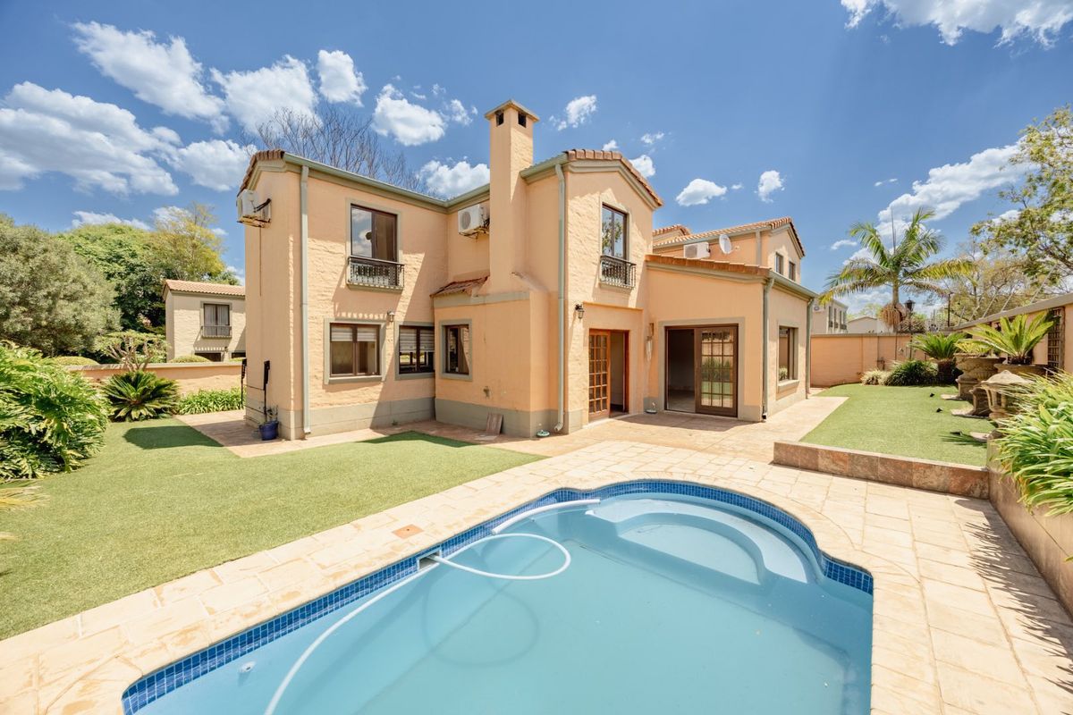 Rear view of the house featuring a swimming pool, paved patio area, landscaped garden, and multi-level exterior facade with chimney and balcony details.