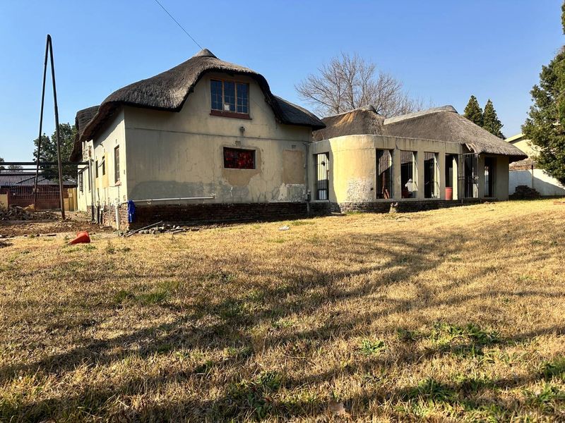 Rear view of a house featuring a traditional thatch roof, security bars on windows, and exterior walls showing significant signs of wear and weathering.