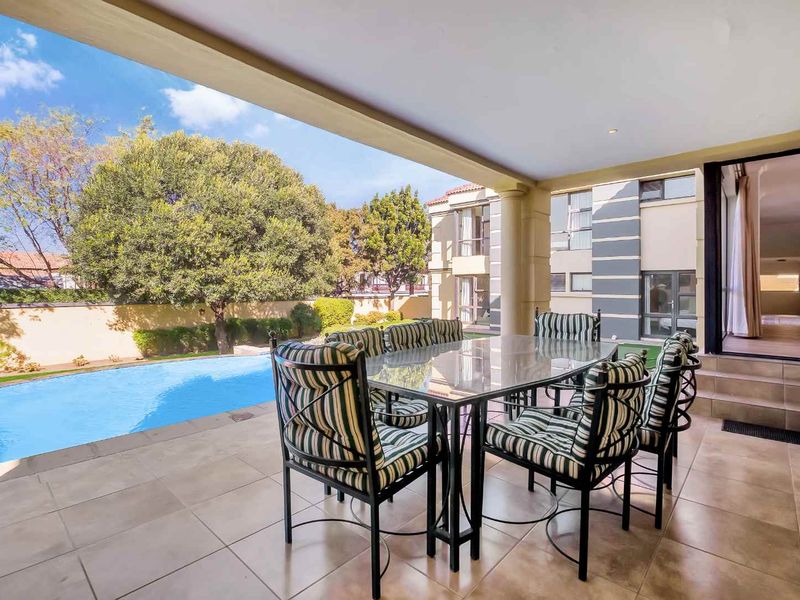 Covered outdoor patio area featuring tiled flooring and recessed lighting, overlooking a private swimming pool and landscaped garden.