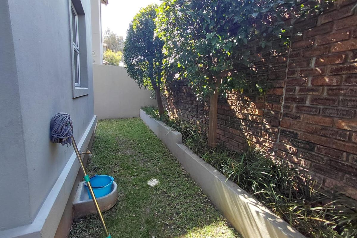 A narrow side garden area featuring a brick boundary wall, a raised planter bed, and an external utility basin with a water tap.