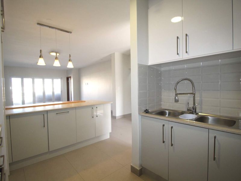Modern open-plan kitchen featuring white cabinetry, subway tile backsplash, double basin sink, and a breakfast bar, flowing into an adjacent living area.