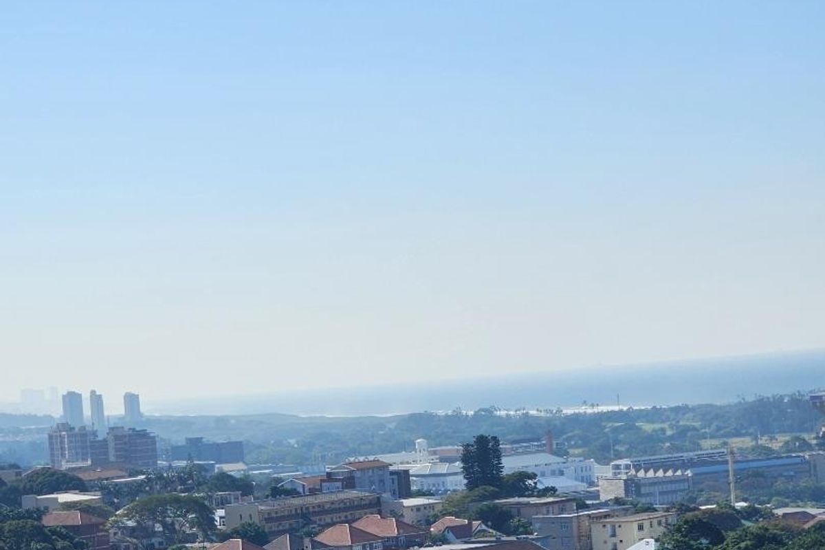 An elevated panoramic view overlooking the surrounding suburban landscape, lush greenery, and distant coastline under a clear blue sky.