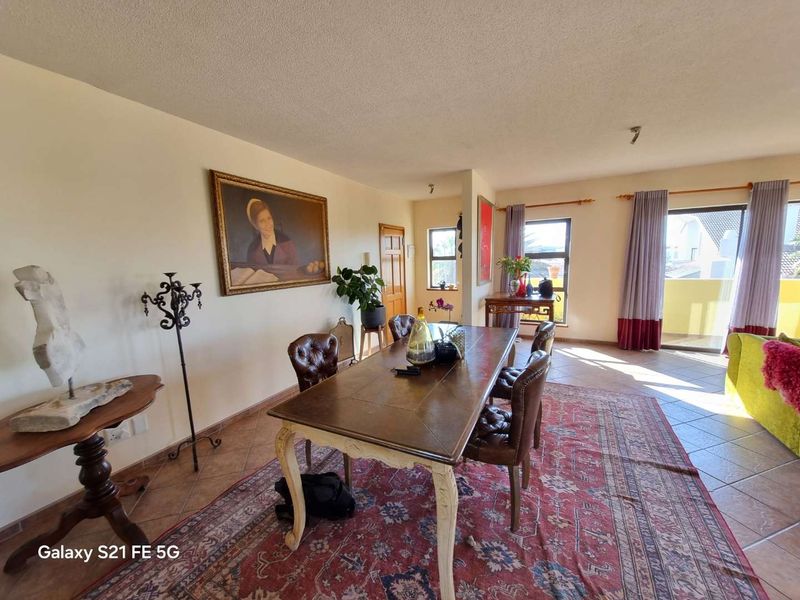 Spacious open-plan living and dining area featuring tiled flooring, natural light from large windows, and direct access to a balcony.