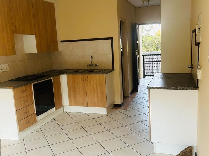 A functional kitchen featuring light wood-finish cabinetry, dark laminate countertops, built-in oven and hob, and tiled flooring, leading out to a balcony area.