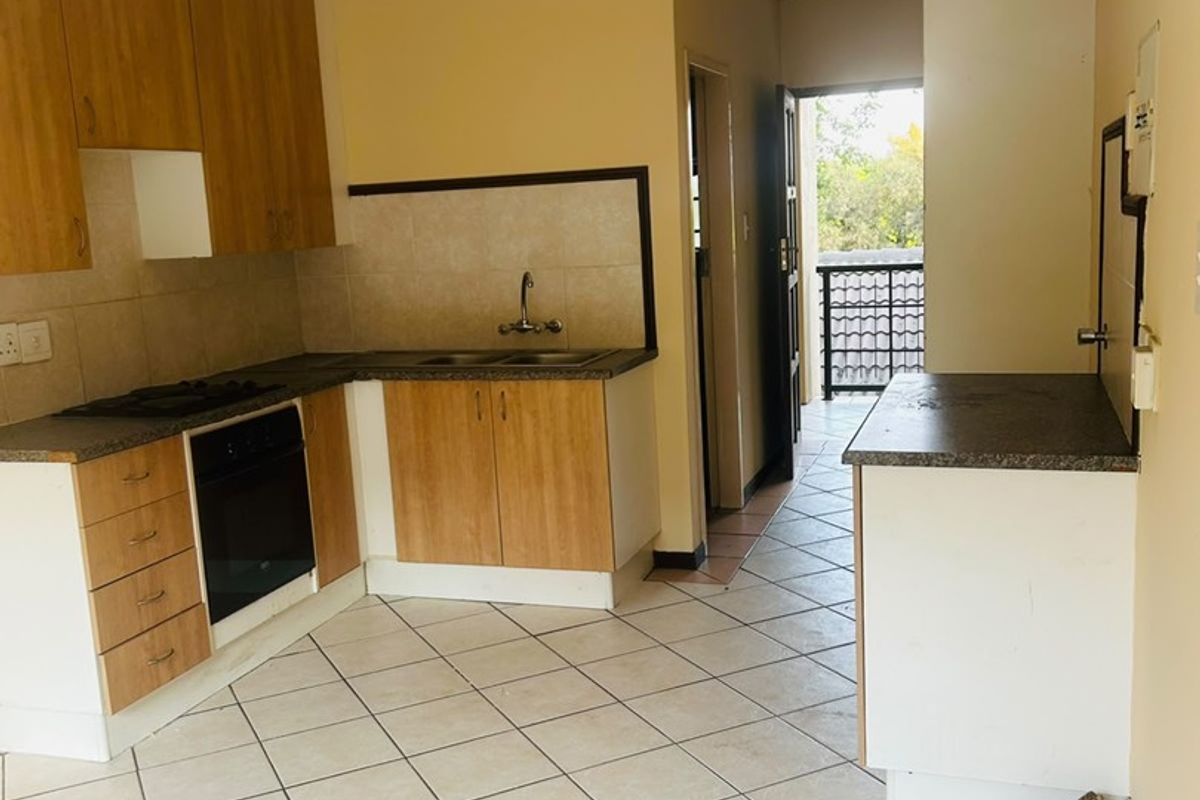 A functional kitchen featuring light wood-finish cabinetry, dark laminate countertops, built-in oven and hob, and tiled flooring, leading out to a balcony area.