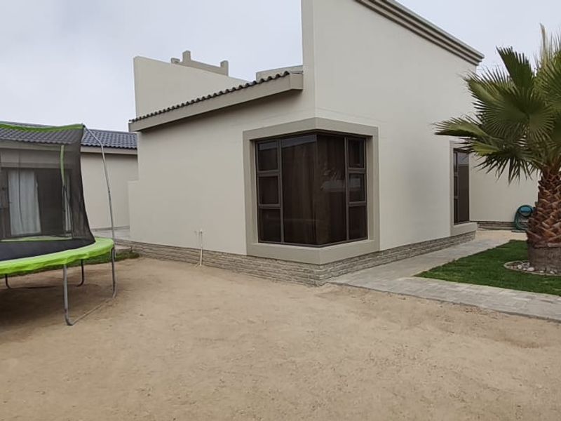 Rear view of the property featuring a modern facade with corner windows, stone cladding accents, and a paved garden walkway.