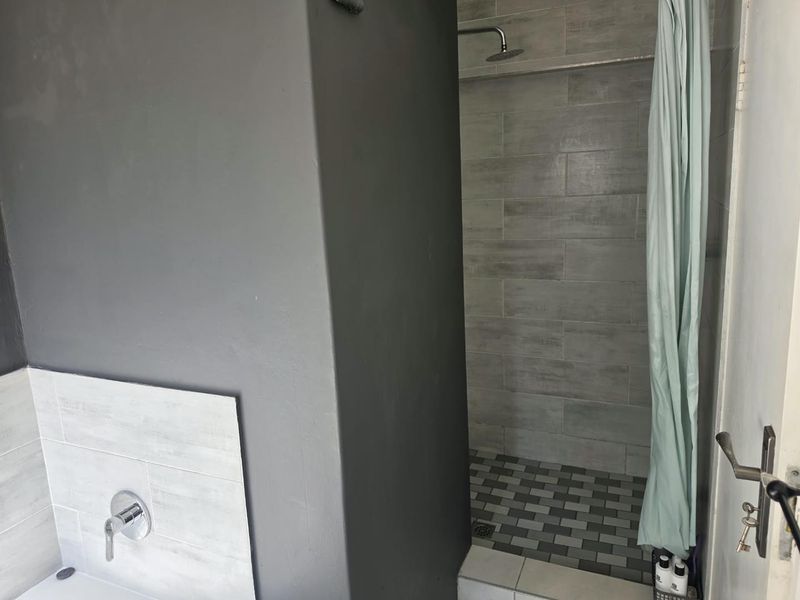 A modern bathroom featuring a walk-in shower with grey tiled walls and a separate bath area with wall-mounted fixtures.