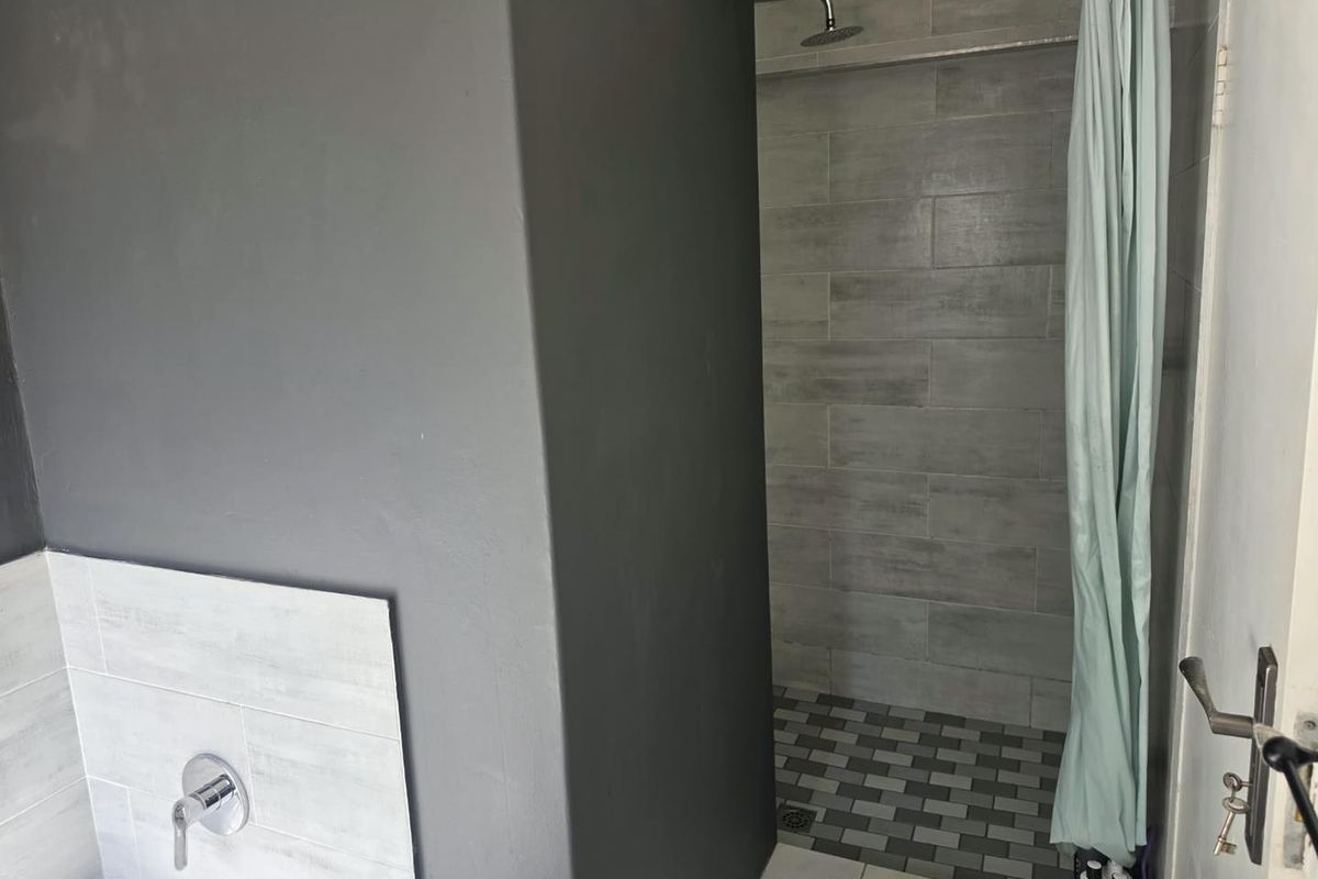 A modern bathroom featuring a walk-in shower with grey tiled walls and a separate bath area with wall-mounted fixtures.