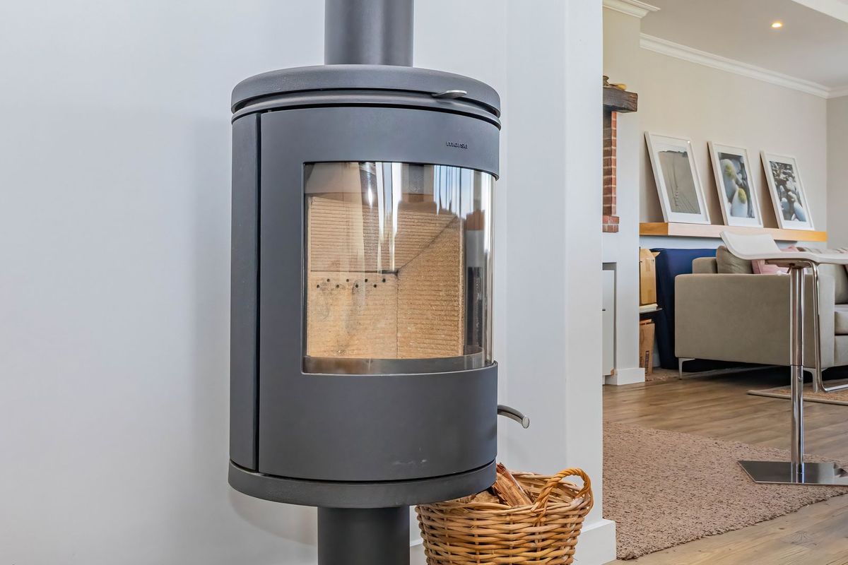 A modern living area featuring a sleek, cylindrical freestanding fireplace as a focal point, complemented by light-toned laminate flooring and recessed ceiling lighting.