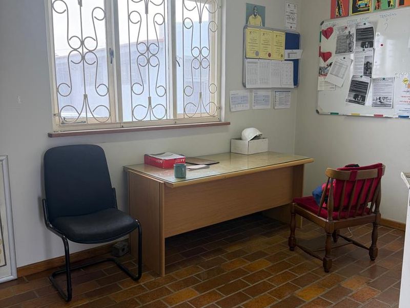 A functional office space featuring terracotta tile flooring and a window fitted with security bars.