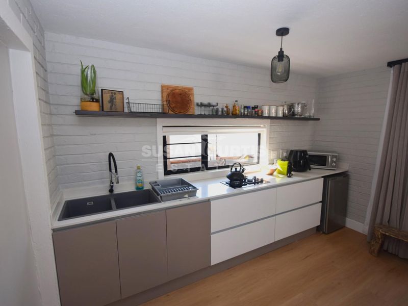 Modern kitchen featuring a double basin sink, built-in hob, floating shelving, and stylish painted brick walls with laminate flooring.
