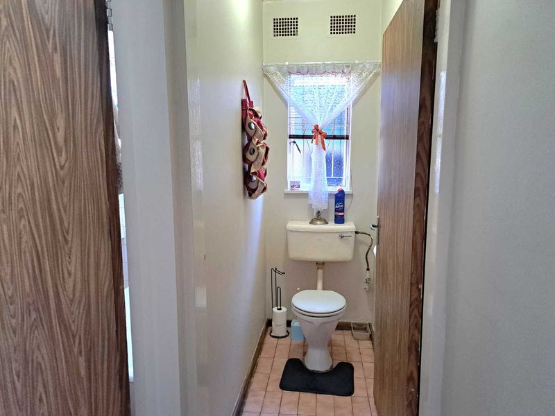 A compact, dated bathroom featuring a standard toilet, tiled flooring, and a window for natural light.