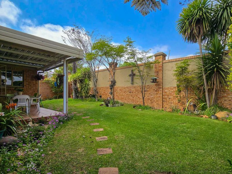 A well-maintained rear garden featuring a covered patio, lush lawn, paved stepping stones, and secure brick boundary walls.
