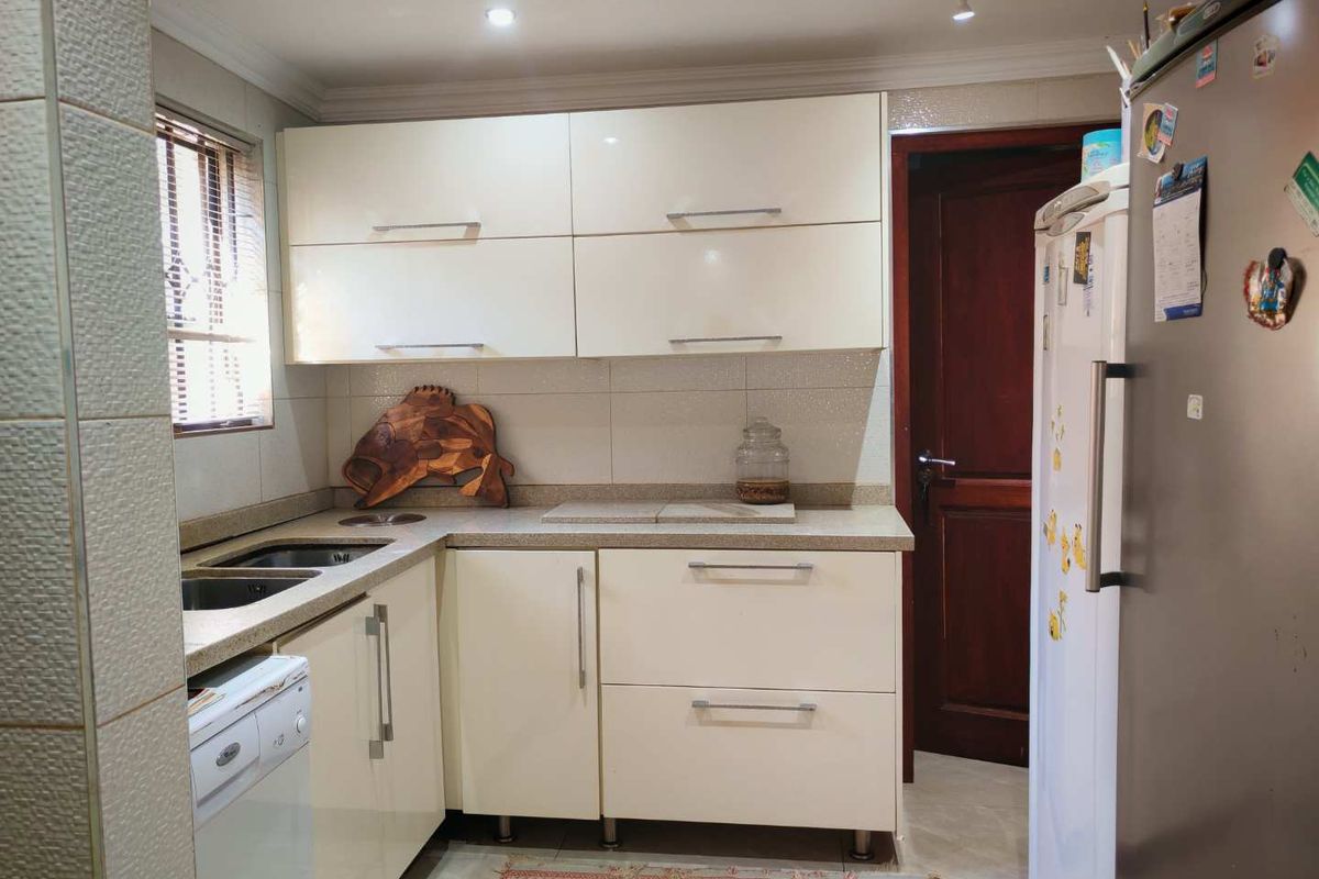 A functional kitchen featuring cream-colored cabinetry, stone-look countertops, a double sink, and tiled splashbacks, providing a practical workspace.