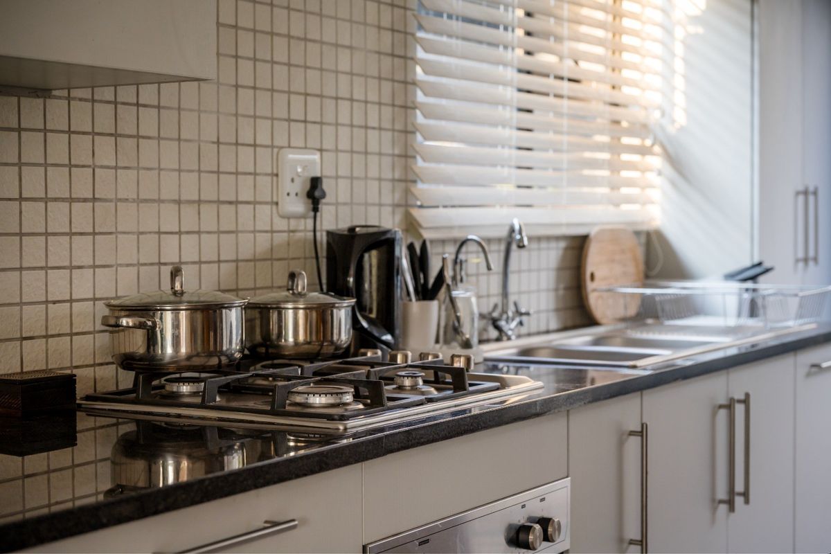 A functional kitchen featuring a gas hob, built-in oven, granite countertops, and a mosaic tile backsplash with natural light from the window.