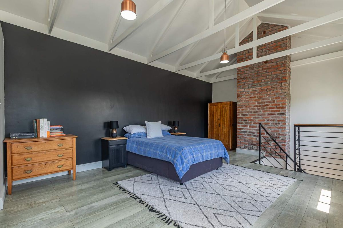 Spacious bedroom featuring a vaulted ceiling with exposed beams, a striking brick chimney breast, and modern wood-look flooring.