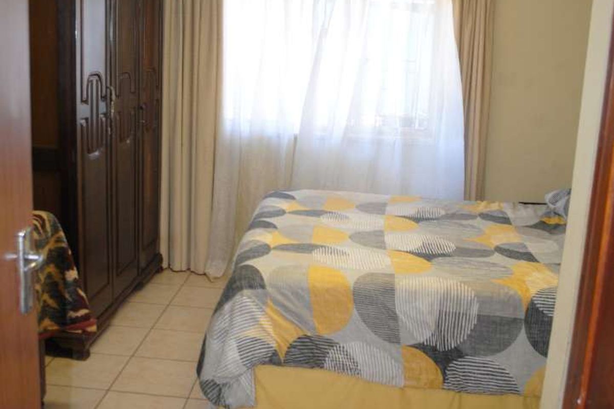 A functional bedroom featuring tiled flooring, a large window with curtaining, and a built-in ceiling light fixture.