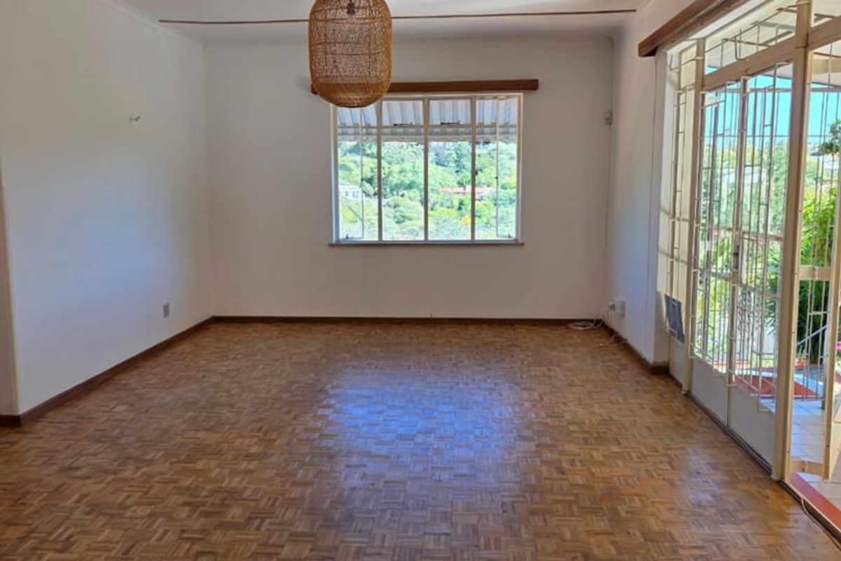 Spacious living area featuring classic parquet flooring, large windows, and direct access to an outdoor patio through sliding glass doors.