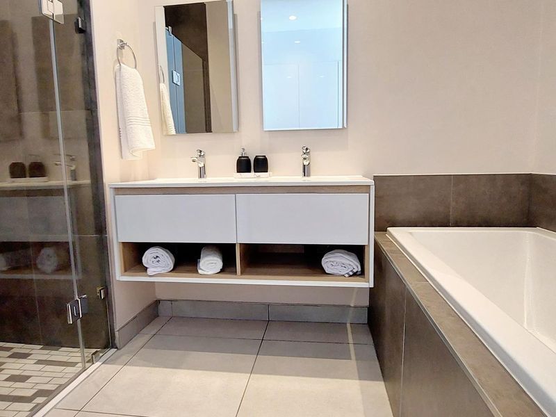 Modern bathroom featuring a double vanity, glass-enclosed shower, and a built-in bathtub with neutral tiled finishes.