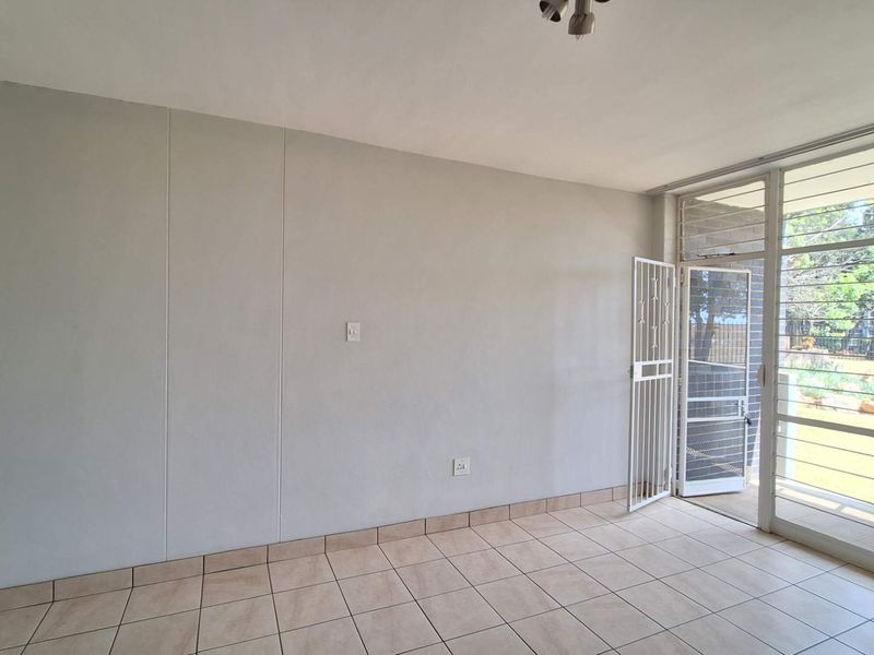 A bright, empty living area featuring neutral tiled flooring and direct access to an outdoor space through a secure sliding glass door.