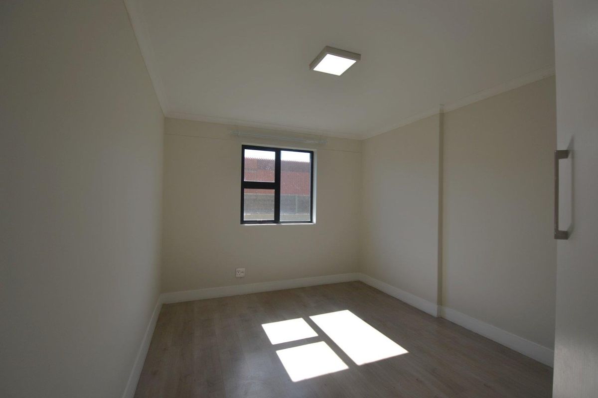 A bright, empty bedroom featuring neutral walls, modern laminate flooring, and a window with dark framing.