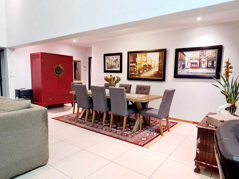 Spacious open-plan living and dining area featuring high double-volume ceilings, neutral tiled flooring, and recessed lighting throughout.