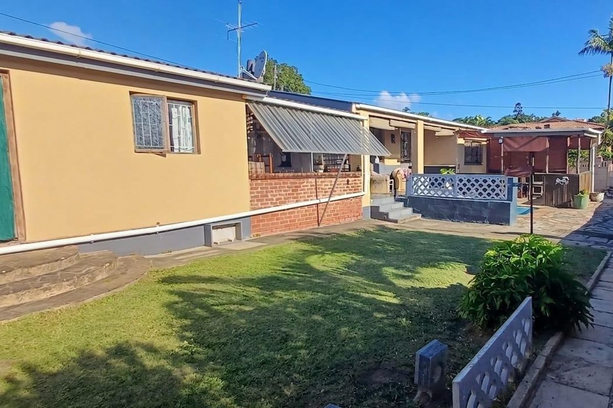 Rear view of the townhouse featuring a private lawn, paved patio area, and an awning over the outdoor living space.