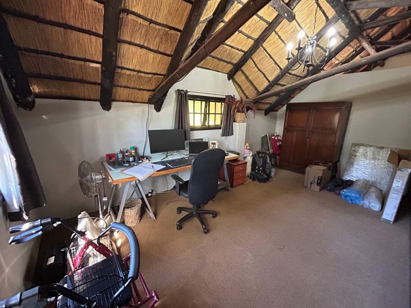 A bedroom featuring a vaulted thatched roof with exposed timber rafters, a built-in wardrobe, and carpeted flooring.