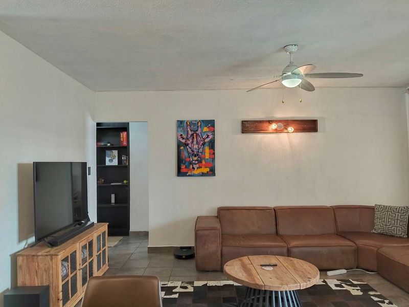 A comfortable living room featuring tiled flooring, a ceiling fan, and built-in shelving, providing a functional and inviting space for relaxation.