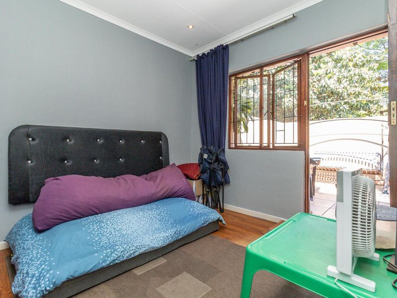A bedroom featuring wooden flooring and direct access to an outdoor patio area through a security-fitted door.