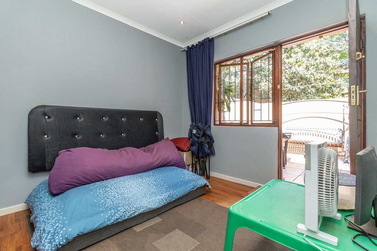 A bedroom featuring wooden flooring and direct access to an outdoor patio area through a security-fitted door.
