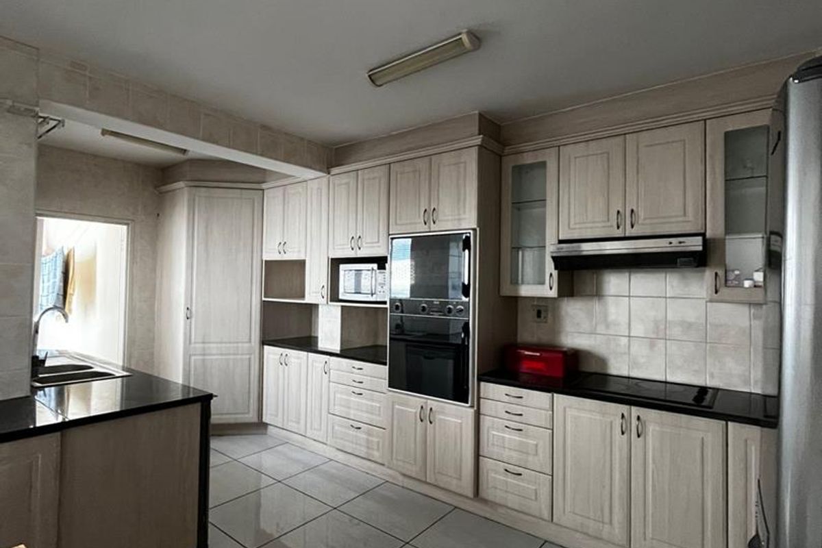 A functional kitchen featuring light-toned cabinetry, dark granite countertops, built-in oven, extractor fan, and tiled flooring throughout.