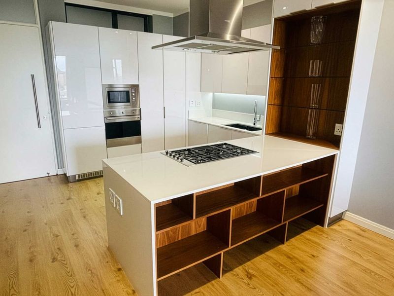 Modern kitchen featuring high-gloss white cabinetry, a central island with a gas hob, built-in appliances, and warm wood-tone shelving and flooring.