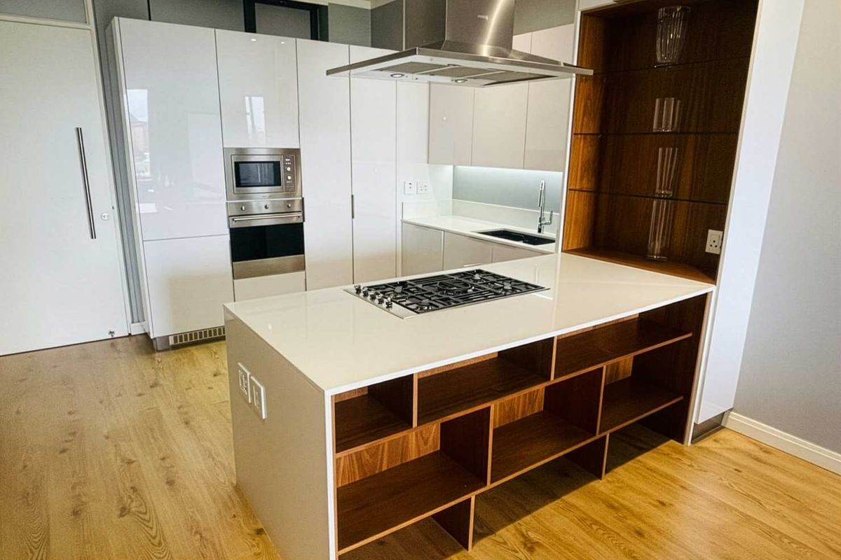 Modern kitchen featuring high-gloss white cabinetry, a central island with a gas hob, built-in appliances, and warm wood-tone shelving and flooring.