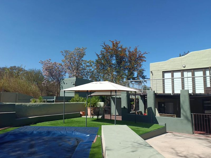 Outdoor pool area featuring an artificial lawn, swimming pool with cover, and a raised balcony with stainless steel balustrades overlooking the garden.