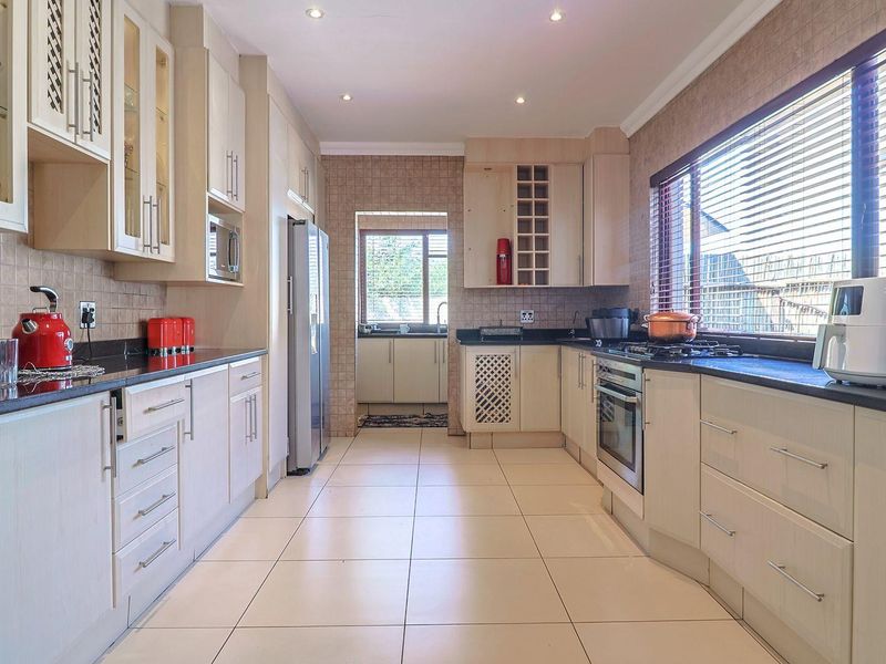 A well-appointed kitchen featuring light-toned cabinetry, granite countertops, built-in oven, gas hob, and a convenient adjoining scullery area with tiled finishes throughout.