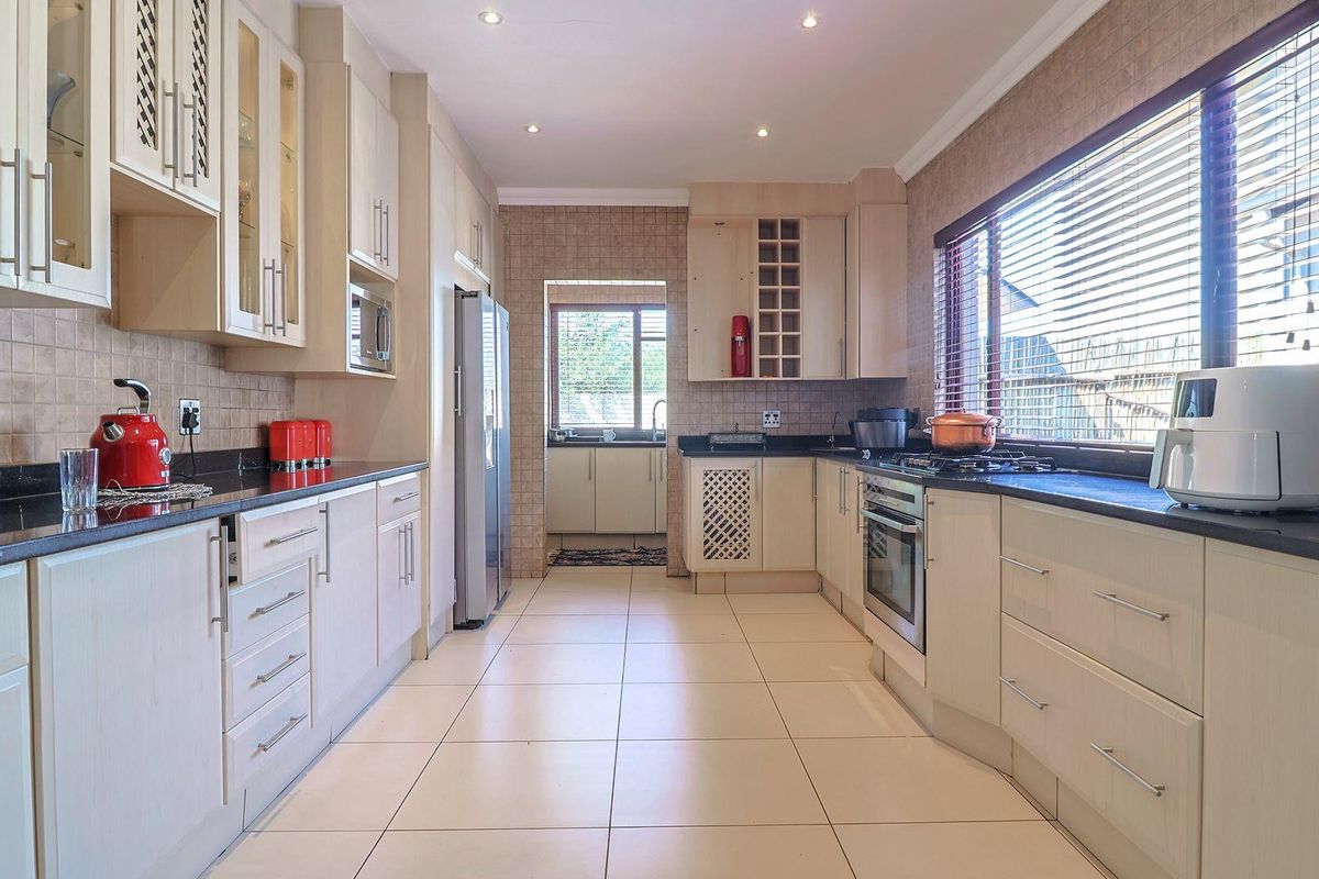A well-appointed kitchen featuring light-toned cabinetry, granite countertops, built-in oven, gas hob, and a convenient adjoining scullery area with tiled finishes throughout.