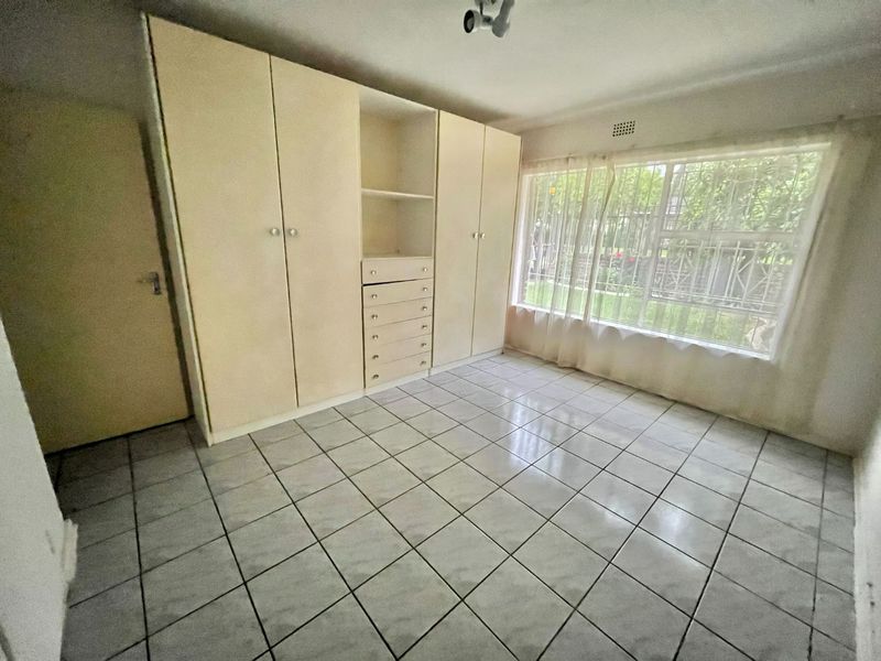 A vacant bedroom featuring built-in cupboards, tiled flooring, and large windows fitted with security bars, offering a blank canvas for personalization.