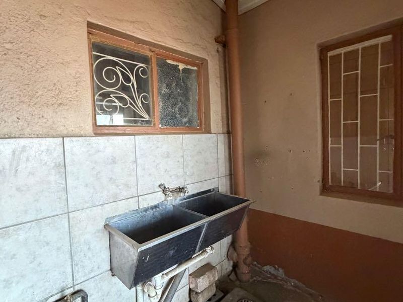 A functional laundry area featuring a stainless steel double sink, tiled splashback, and exposed plumbing, requiring maintenance and cosmetic updates.