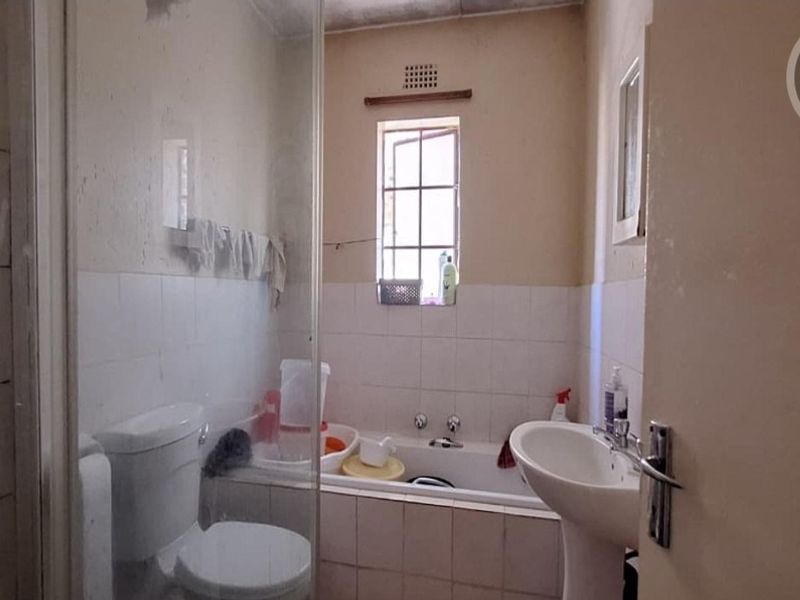 A dated bathroom featuring a pedestal basin, built-in bathtub, and a glass shower screen, requiring cosmetic updates to modernize the space.
