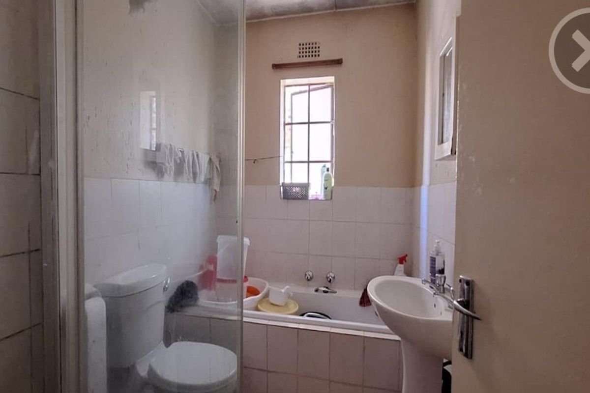 A dated bathroom featuring a pedestal basin, built-in bathtub, and a glass shower screen, requiring cosmetic updates to modernize the space.