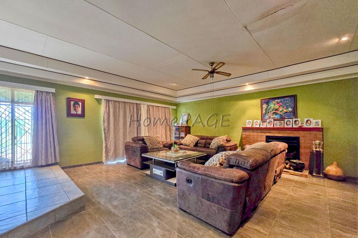Spacious living room featuring a brick fireplace, tiled flooring, and a tray ceiling with a central fan.