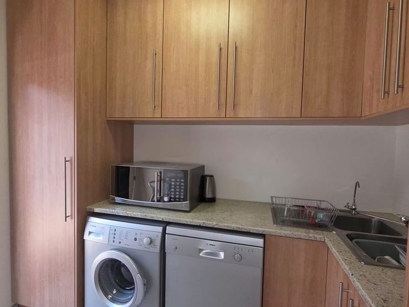 A functional laundry area featuring wood-finish cabinetry, stone countertops, and dedicated spaces for a washing machine and dishwasher.