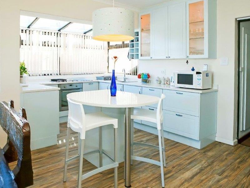 A bright, functional kitchen featuring light blue cabinetry, integrated appliances, a central breakfast nook, and wood-look laminate flooring.