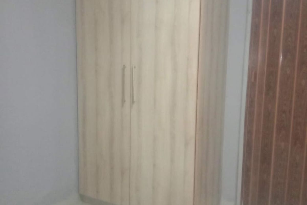 A clean, empty bedroom featuring light wood-finish built-in wardrobes, neutral grey walls, and tiled flooring.