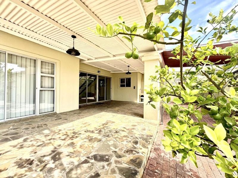 A spacious covered patio featuring stone paving, built-in braai, and direct access to the interior through large sliding glass doors.