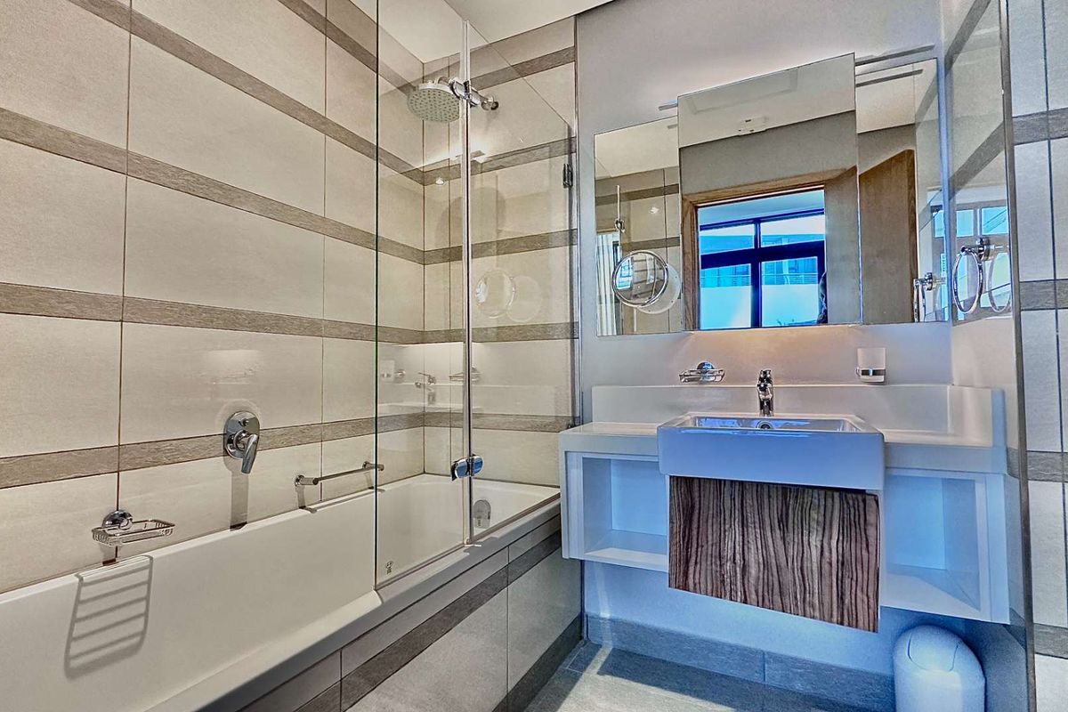 Modern bathroom featuring a wall-mounted vanity with integrated basin, a bathtub with a glass shower screen, and contemporary tiled walls.