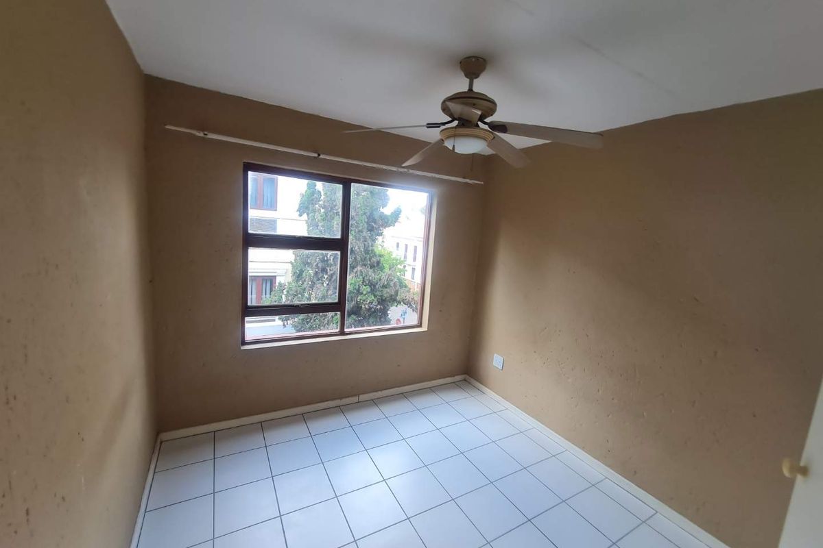 An empty bedroom featuring tiled flooring, a ceiling fan, and a large window with an aluminium frame.