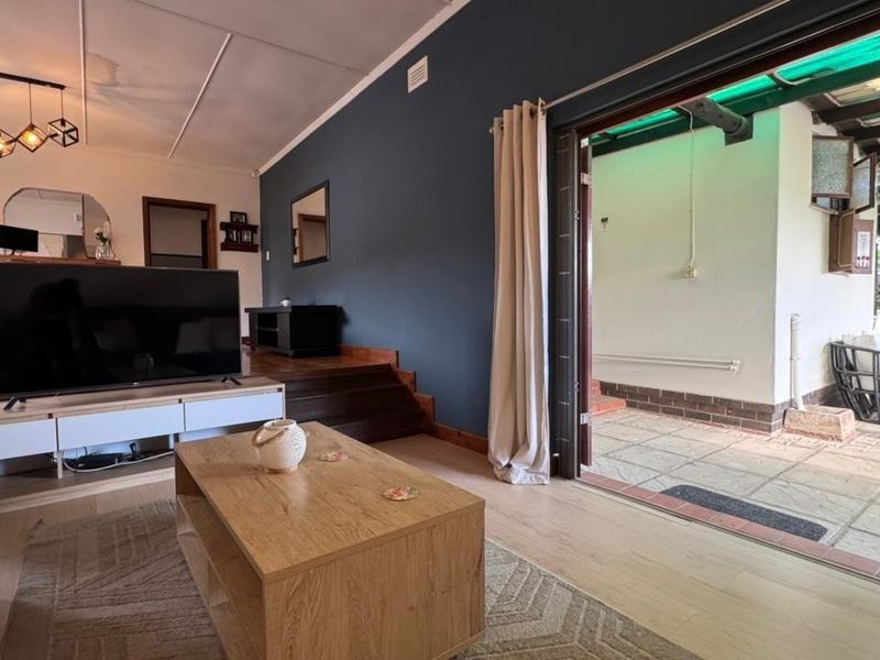 A living room featuring laminate flooring, a dark accent wall, and a sliding door providing direct access to an outdoor patio area.